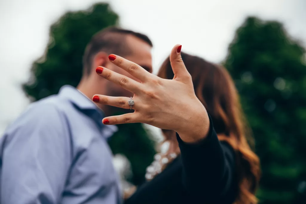 Image of an engagement ring in focus with hand covering couple's faces